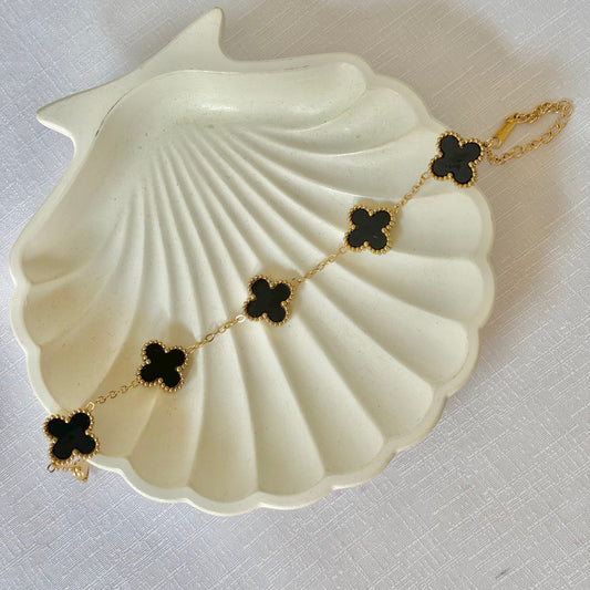 Gold bracelet with black clover-shaped charms on a white shell